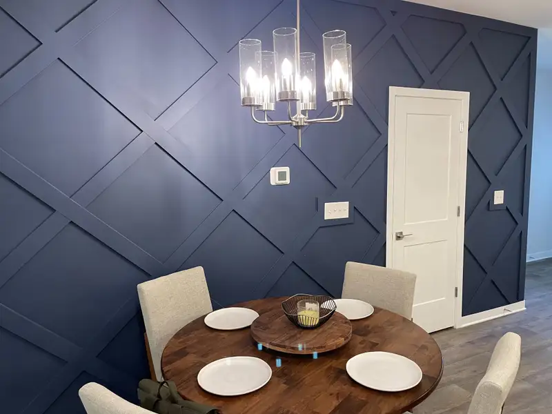A chic dining area featuring a round wooden table, modern chandelier, and blue accent wall with geometric patterns. A chic dining area featuring a round wooden table, modern chandelier, and blue accent wall with geometric patterns.