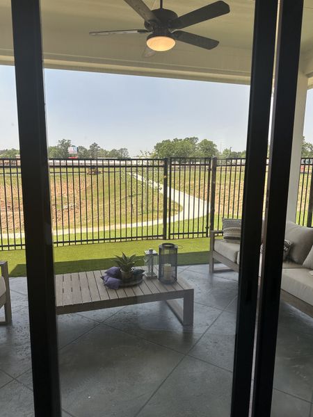 A cozy patio with modern furniture, a ceiling fan, and views of a landscaped lawn through sleek railings.