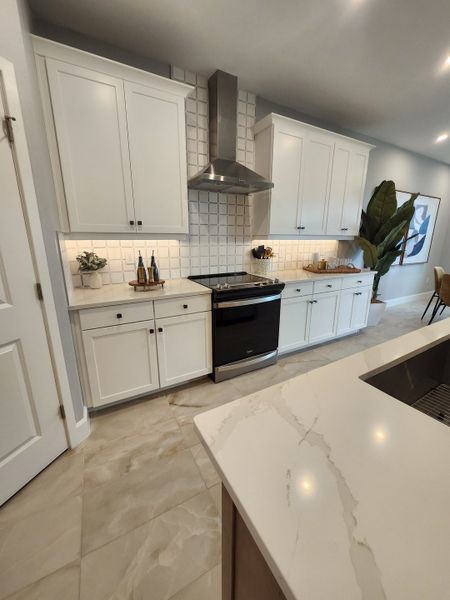 A modern kitchen featuring white cabinets, elegant tile backsplash, and a sleek marble-topped island.