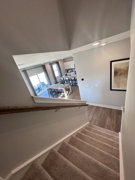 A cozy staircase with plush carpet leads to a bright dining area with modern table and large windows.