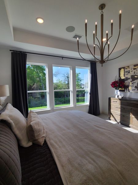 A bright bedroom with large windows, elegant chandelier, dark curtains, and cozy bedding, complemented by stylish decor.