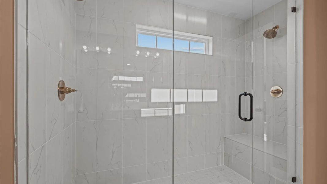 Stunning marble tiled walk-in frameless shower with bench seat and gold accents at Pelham Crossing in Greenville, SC