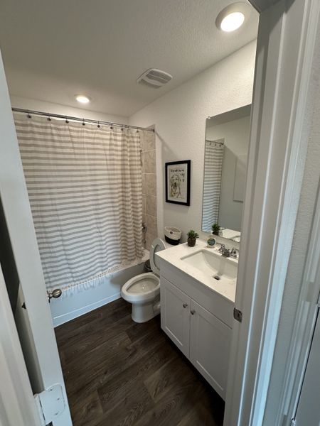 A cozy bathroom featuring a white vanity, stylish fixtures, and a neutral shower curtain, creating a clean and inviting space.