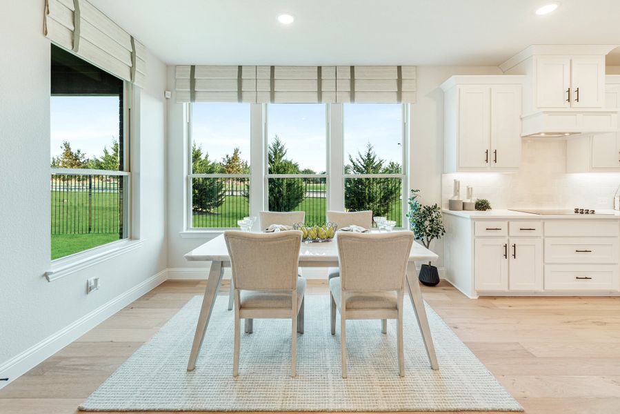 Bright dining area with white table, four chairs, large windows, and adjacent white kitchen cabinets on light hardwood floors. Bright dining area with white table, four chairs, large windows, and adjacent white kitchen cabinets on light hardwood floors.