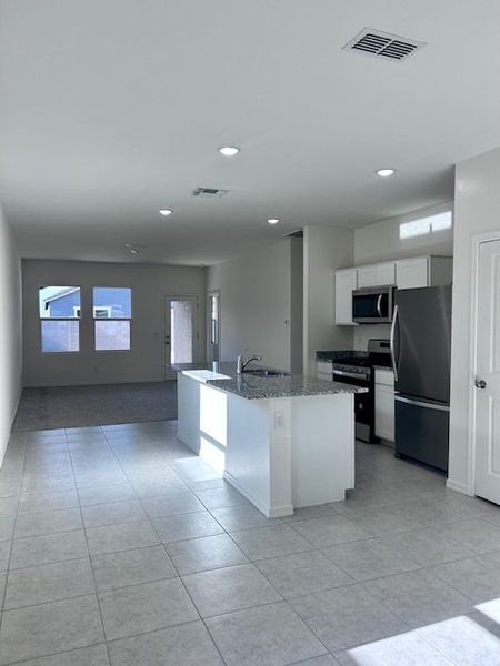 A modern kitchen with sleek appliances, granite countertops, and tiled floors opens into a spacious living area.