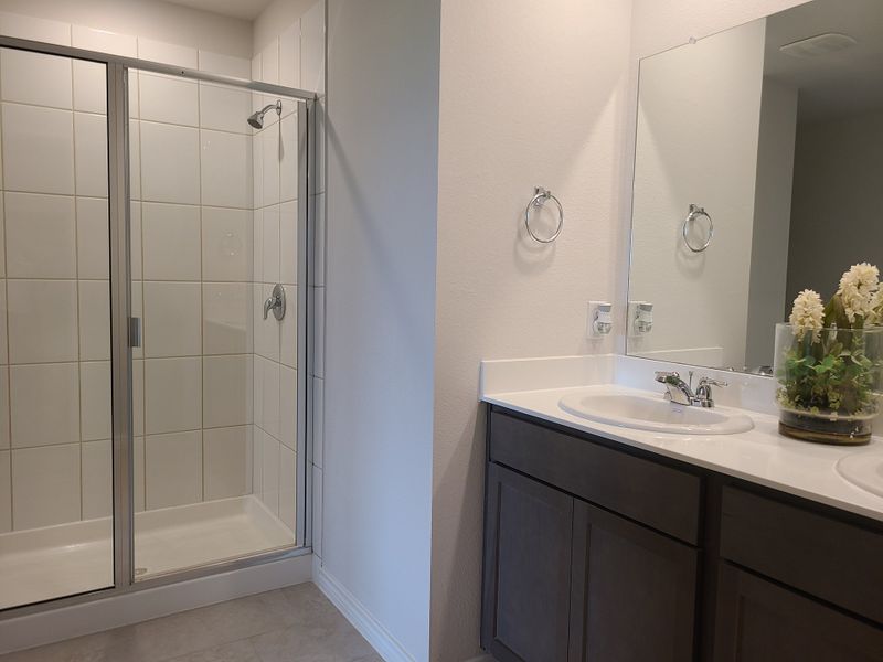 A modern bathroom with a glass-enclosed shower, sleek dark vanity, and elegant floral decor.