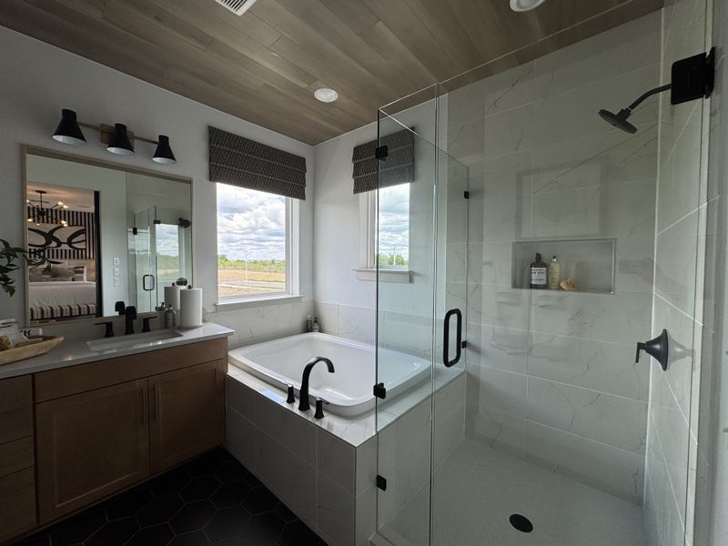 A chic bathroom features a glass shower, elegant tub, and stylish vanity with wooden accents and modern fixtures.