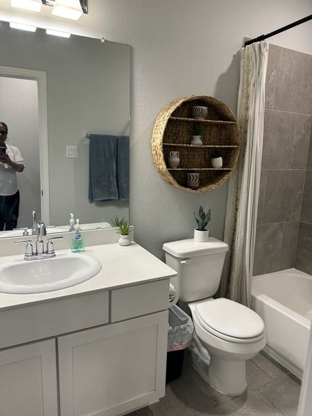 A modern bathroom with a sleek vanity, round woven shelf, and elegant tiled shower. A modern bathroom with a sleek vanity, round woven shelf, and elegant tiled shower.
