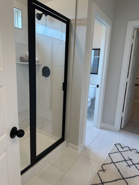 A modern bathroom featuring a sleek black-framed glass shower and glossy tiled floor.