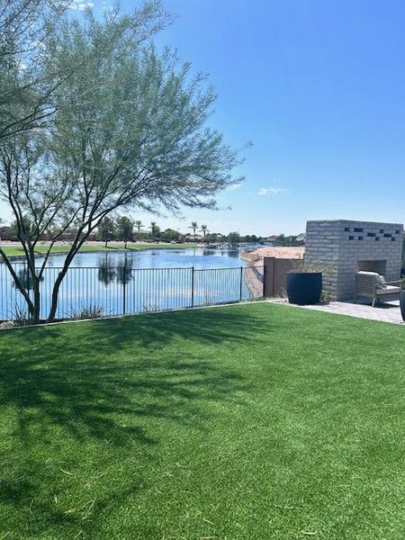 A serene backyard with lush grass, a tree, and a view of the lake in Seasons at Rancho El Dorado IV by Richmond American Homes.