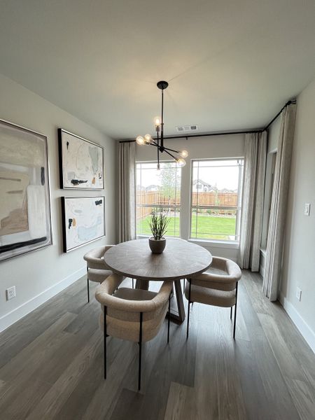 A modern dining area featuring a round table, elegant chairs, abstract art, and large windows with garden views. A modern dining area featuring a round table, elegant chairs, abstract art, and large windows with garden views.