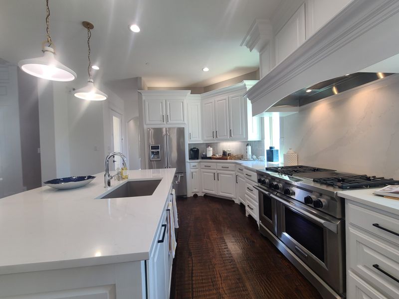 A spacious kitchen with white cabinetry, a large island, stainless steel appliances, and modern pendant lighting. A spacious kitchen with white cabinetry, a large island, stainless steel appliances, and modern pendant lighting.