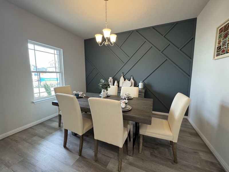 A chic dining room with a dark accent wall, elegant chandelier, and cream chairs around a wooden table.