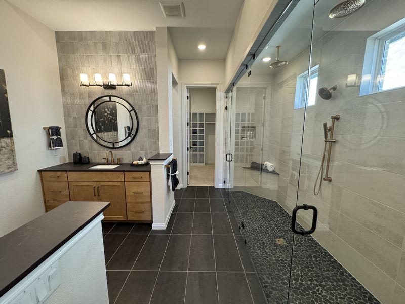 A modern bathroom featuring a glass shower with pebble flooring, sleek wood vanity, and round mirror with elegant lighting.