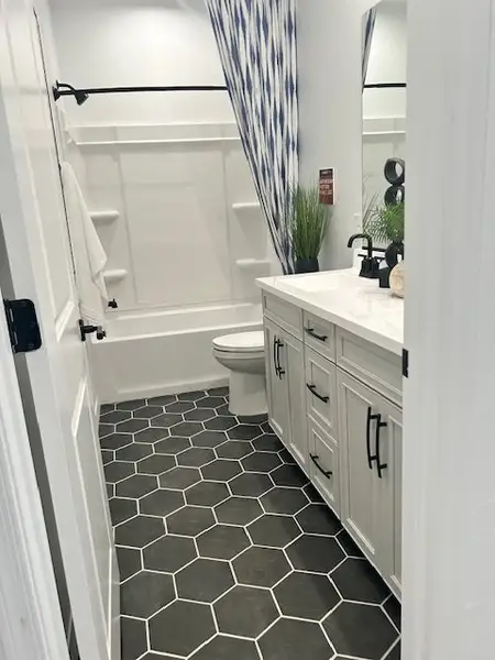 A modern bathroom with hexagonal black tiles, white vanity, and a tiled shower/tub combo with a patterned curtain.