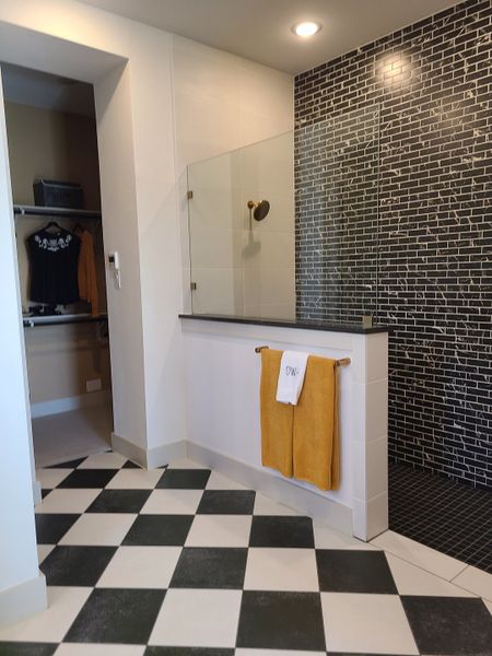 A chic bathroom with a black and white checkered floor, glass shower, and stylish black brick wall accents.