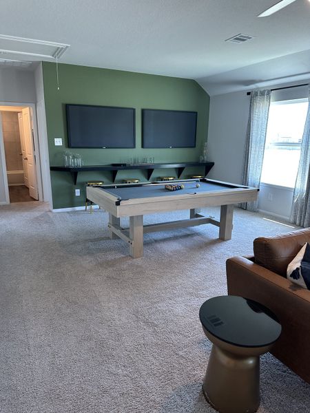 A cozy game room featuring a stylish pool table, dual TVs, and comfy seating, perfect for entertainment and relaxation.