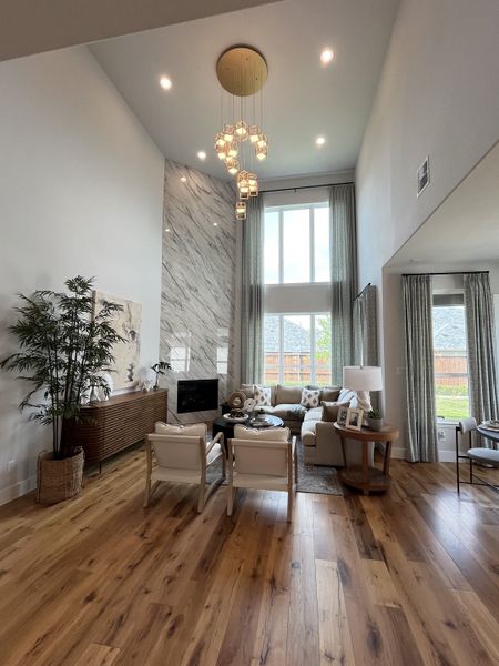 A spacious living room featuring a marble accent wall, elegant chandelier, and large windows with serene views.