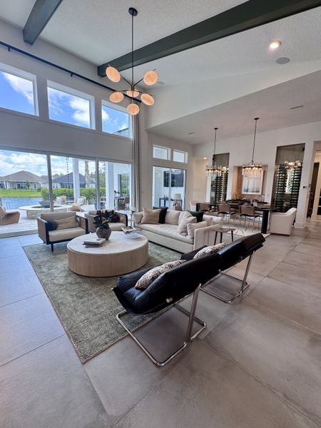 A modern open living area with high ceilings, large windows, chic light fixtures, and elegant furnishings.
