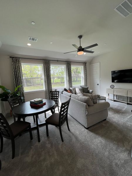 A cozy living area with a gray sofa, elegant dining set, large windows, and a ceiling fan, offering comfort and style.