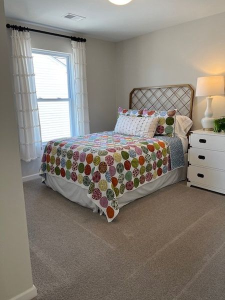 A cozy bedroom with a colorful quilt, elegant lattice headboard, and soft natural light from a large window.