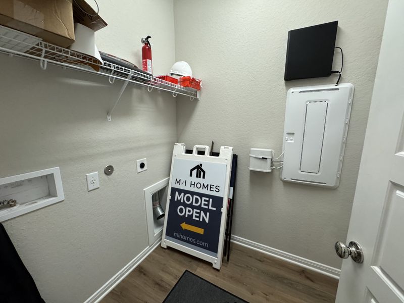 A functional utility room with storage shelving and modern paneling, featuring a promotional sign for M/I Homes.