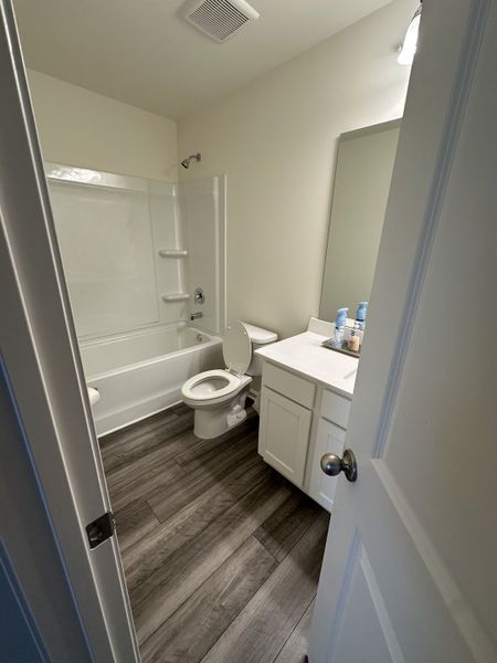 A compact bathroom with elegant wood-look flooring, a sleek vanity, and a pristine white bathtub.
