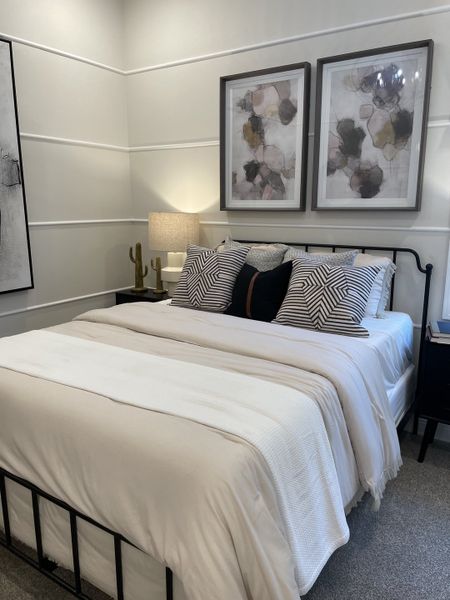 A cozy bedroom featuring a stylish black metal bed frame, plush pillows, abstract art, and soft lighting for a relaxing ambiance.