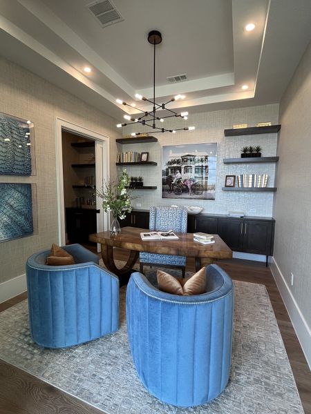 A cozy study with blue velvet chairs, chic shelves, and modern lighting.