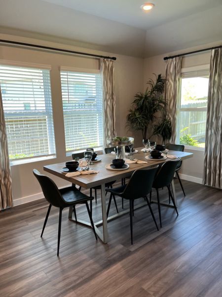 A cozy dining area with a modern table setting, elegant chairs, and ample natural light from large windows.
