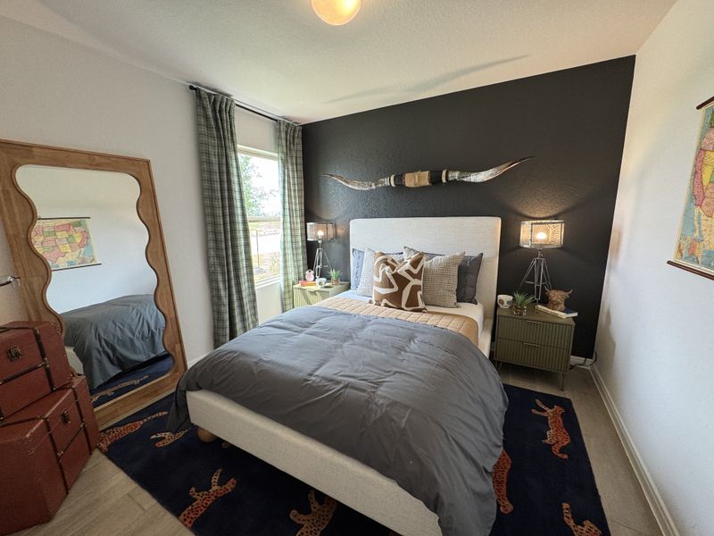 A cozy bedroom with a dark accent wall, stylish bedding, and eclectic decor including maps and a decorative horn.