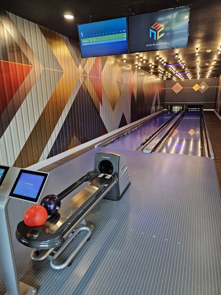 A sleek bowling alley with patterned walls, modern lighting, and interactive screens for an entertaining experience.