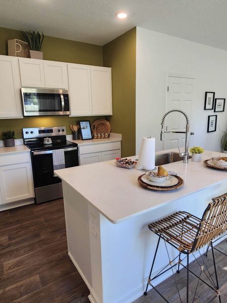 A modern kitchen featuring white cabinets, olive accent wall, and sleek appliances with a chic breakfast bar.