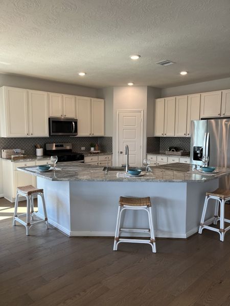 A modern kitchen with white cabinets, granite countertops, and a spacious island with stools.