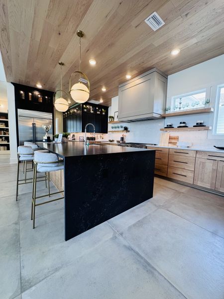 A contemporary kitchen featuring elegant pendant lighting, sleek black island, and natural wood cabinetry with open shelving.