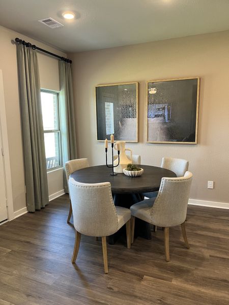 A cozy dining area with a round table, elegant chairs, wood flooring, modern art, and soft drapes for a warm ambiance.