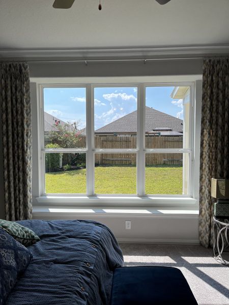 A cozy bedroom with a large window, natural light, and elegant curtains overlooking a sunny backyard. A cozy bedroom with a large window, natural light, and elegant curtains overlooking a sunny backyard.