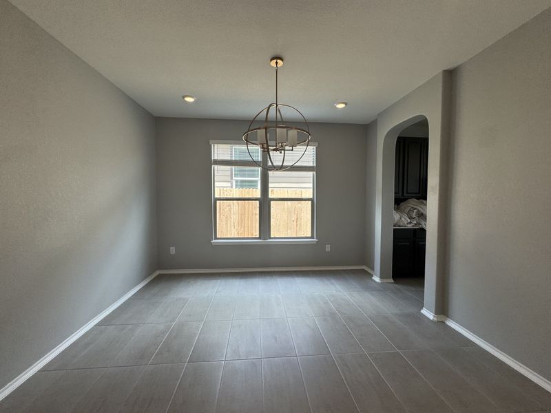 A modern dining room with gray walls, large tiles, and an elegant chandelier.