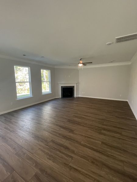 A spacious living room with wood flooring, a cozy fireplace, and ceiling fan, bathed in natural light from large windows.