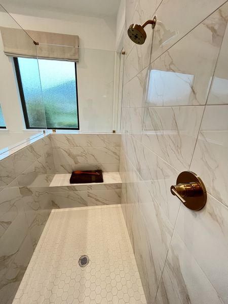 A sleek shower with marble-patterned tiles, hexagonal floor design, and brushed brass fixtures offers a modern, elegant touch.