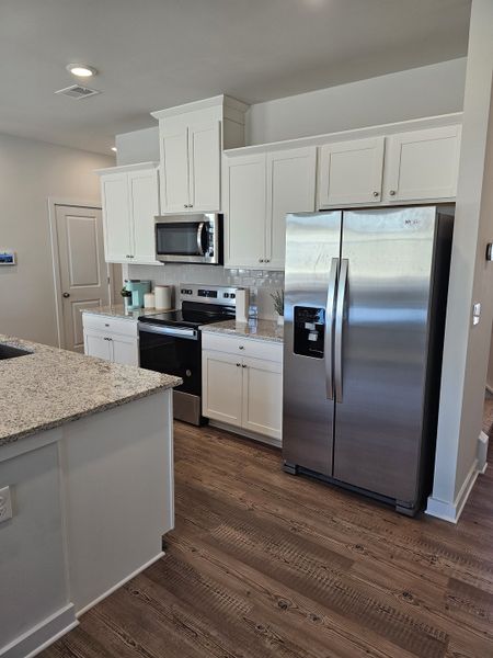 A modern kitchen featuring white cabinetry, granite countertops, stainless steel appliances, and sleek wood flooring. A modern kitchen featuring white cabinetry, granite countertops, stainless steel appliances, and sleek wood flooring.