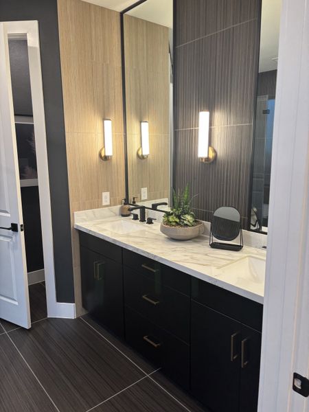 Elegant bathroom with dual black vanity, marble countertop, vertical sconces, and modern wall tile accents. Elegant bathroom with dual black vanity, marble countertop, vertical sconces, and modern wall tile accents.