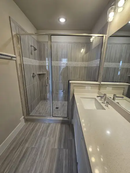 A modern bathroom featuring a spacious glass shower, sleek vanity with a quartz countertop, and elegant gray tile flooring.
