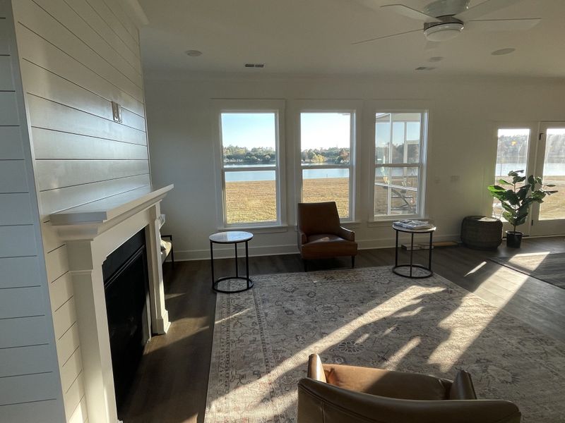 A cozy living room with a shiplap fireplace, leather chairs, and large windows offering a serene lakeside view.