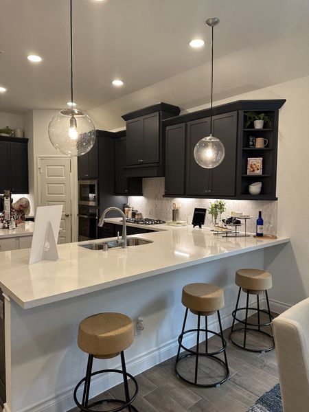 A modern kitchen with sleek dark cabinets, a white island, and stylish pendant lighting above bar stools.