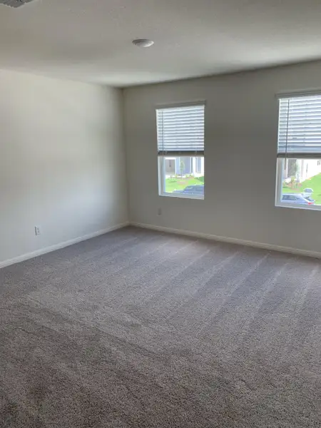 A bright, carpeted room with two windows and neutral walls, offering a cozy and inviting ambiance.