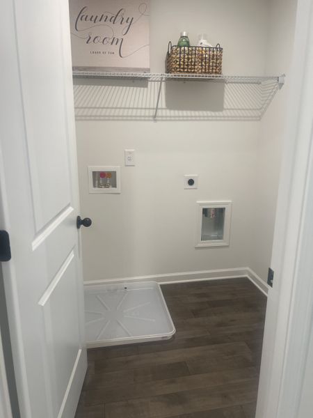 A cozy laundry room with dark wood flooring, wire shelving, and a decorative sign adding charm and functionality. A cozy laundry room with dark wood flooring, wire shelving, and a decorative sign adding charm and functionality.