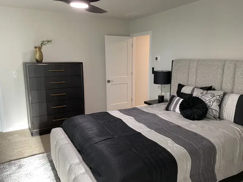 A cozy bedroom with a stylish striped bedspread, plush headboard, and sleek black dresser. A cozy bedroom with a stylish striped bedspread, plush headboard, and sleek black dresser.