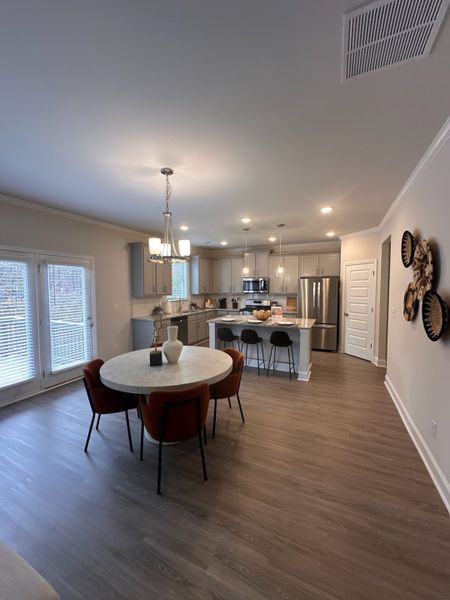 A modern kitchen with a round dining table, sleek cabinets, and pendant lighting, featuring stylish decor on wood flooring.