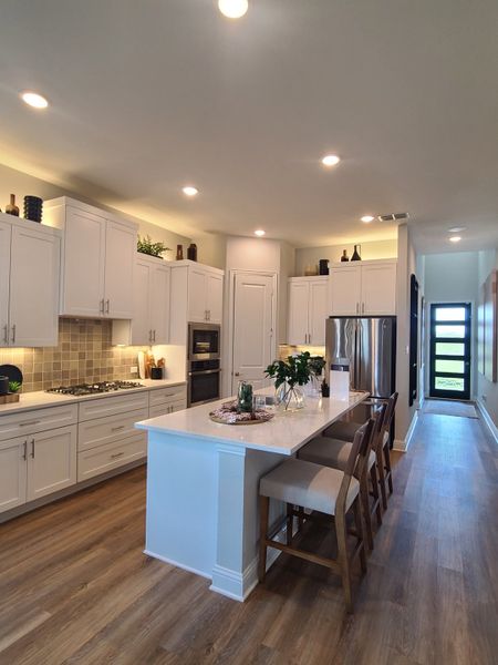 A modern kitchen featuring sleek white cabinets, a spacious island with seating, and elegant wood flooring.